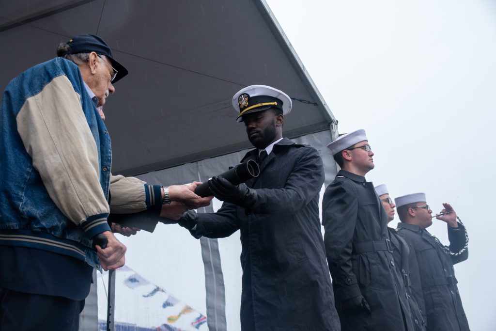BURNS HARBOR, Ind. (Oct. 26, 2019) Dick Thelen, a veteran seaman 2nd class and a survivor of the sinking of USS Indianapolis (CA 35), hands the long glass (telescope) to Lt. Julian Turner, navigator of the first watch, during the commissioning ceremony of USS Indianapolis (LCS 17). LCS 17 is the 19th littoral combat ship to enter the fleet and the ninth of the Freedom variant. It will be the fourth ship named for Indianapolis, Indiana's capital city. (U.S. Navy photo by Mass Communication Specialist 3rd Class Timothy Haggerty)