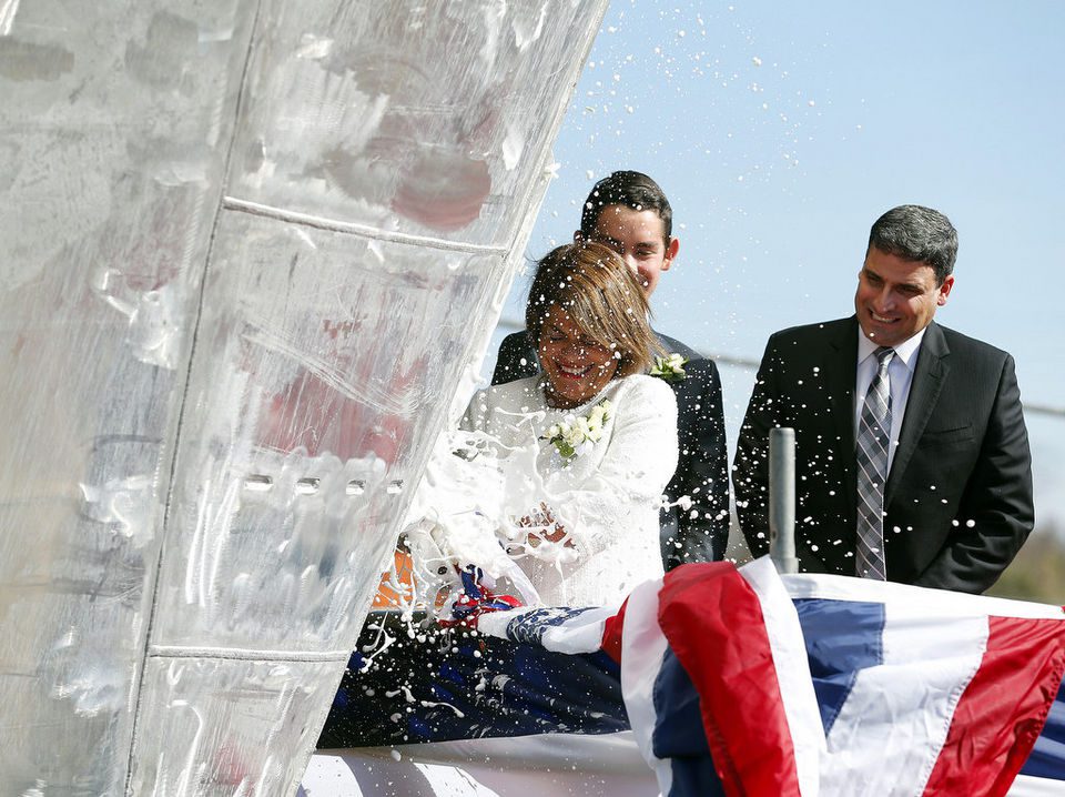 Woman smashing champagne bottle at ceremony.